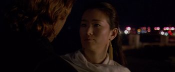 Movie still from “Miami Vice” (2006), directed by Michael Mann – A young woman wearing a white shirt and gold earrings; Close Up shot, Over the shoulder angle