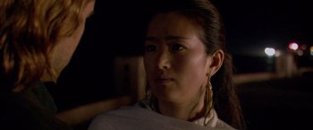 Movie still from “Miami Vice” (2006), directed by Michael Mann – A young woman wearing a white shirt and a pair of gold earrings; Close Up shot, Over the shoulder angle