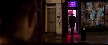 Movie still from “Last Night in Soho” (2021), directed by Edgar Wright – A man standing in front of a building at night; Wide shot, Over the shoulder angle