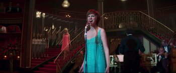 Movie still from “Last Night in Soho” (2021), directed by Edgar Wright – A woman singing into a microphone in front of a staircase; Wide shot, Low angle