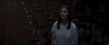 Movie still from “Last Night in Soho” (2021), directed by Edgar Wright – A woman standing in a room with many wooden chairs; Medium shot, High angle