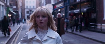 Movie still from “Last Night in Soho” (2021), directed by Edgar Wright – A woman in a white jacket walking down a street; Close Up shot, Over the shoulder angle