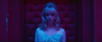 Movie still from “Last Night in Soho” (2021), directed by Edgar Wright – A woman with blonde hair and a white dress in front of a purple wall; Close Up shot, Low angle