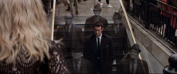 Movie still from “Last Night in Soho” (2021), directed by Edgar Wright – A man in a suit and tie standing on some stairs; Wide shot, Over the shoulder angle