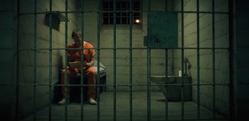 Movie still from “Midnight Mass” (2021), directed by Mike Flanagan – A man in an orange jumpsuit sitting in a jail cell; Wide shot, High angle