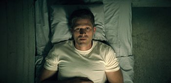 Movie still from “Midnight Mass” (2021), directed by Mike Flanagan – A man laying in a bed in a white shirt; Close Up shot, High angle