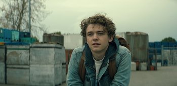 Movie still from “Midnight Mass” (2021), directed by Mike Flanagan – A young man with a backpack is posing for a picture; Close Up shot, Low angle