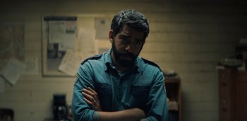 Movie still from “Midnight Mass” (2021), directed by Mike Flanagan – A man with his arms crossed in front of a wall; Close Up shot, High angle