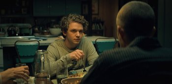 Movie still from “Midnight Mass” (2021), directed by Mike Flanagan – A man sitting at a dinner table eating food; Medium shot, Over the shoulder angle