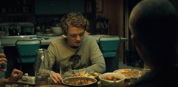 Movie still from “Midnight Mass” (2021), directed by Mike Flanagan – A man sitting at a table with a plate of food; Medium shot, Over the shoulder angle