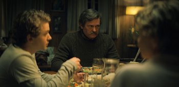 Movie still from “Midnight Mass” (2021), directed by Mike Flanagan – A man sitting at a table with a glass of wine; Medium shot, Over the shoulder angle