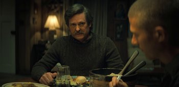 Movie still from “Midnight Mass” (2021), directed by Mike Flanagan – A man sitting at a table with a bowl of food; Medium shot, Over the shoulder angle