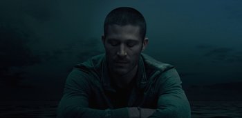 Movie still from “Midnight Mass” (2021), directed by Mike Flanagan – A man with his arms crossed sitting in the dark; Close Up shot, Low angle