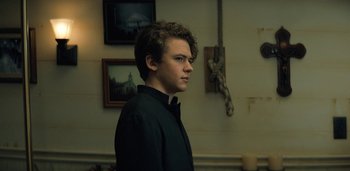 Movie still from “Midnight Mass” (2021), directed by Mike Flanagan – A young man standing in a room next to candles; Medium shot, Low angle