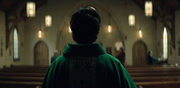 Movie still from “Midnight Mass” (2021), directed by Mike Flanagan – A person wearing a green robe in front of an altar; Medium shot, Low angle