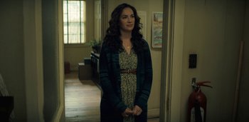 Movie still from “Midnight Mass” (2021), directed by Mike Flanagan – A woman standing in front of a window in a room; Medium shot, Over the shoulder angle