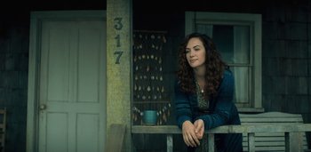 Movie still from “Midnight Mass” (2021), directed by Mike Flanagan – A woman sitting on top of a wooden railing; Medium shot, Low angle