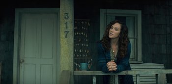 Movie still from “Midnight Mass” (2021), directed by Mike Flanagan – A woman leaning on a railing in front of a house; Medium shot, Low angle