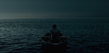 Movie still from “Midnight Mass” (2021), directed by Mike Flanagan – A man sitting in a boat in the middle of the ocean; Extreme Wide shot, High angle