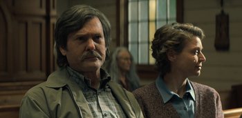 Movie still from “Midnight Mass” (2021), directed by Mike Flanagan – A man with a beard and mustache standing next to a woman with long hair; Close Up shot, Over the shoulder angle