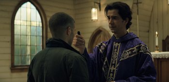 Movie still from “Midnight Mass” (2021), directed by Mike Flanagan – A man in a priest's robe is talking to another man in a green jacket; Close Up shot, Over the shoulder angle
