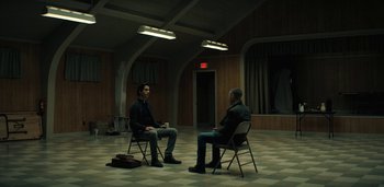 Movie still from “Midnight Mass” (2021), directed by Mike Flanagan – Two men are sitting in chairs in an empty room; Wide shot, High angle