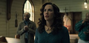 Movie still from “Midnight Mass” (2021), directed by Mike Flanagan – A woman standing in front of two other people in a room; Close Up shot, Low angle