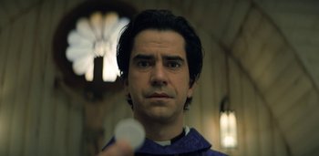 Movie still from “Midnight Mass” (2021), directed by Mike Flanagan – A man in a priest's robe holding a paper; Close Up shot, Low angle