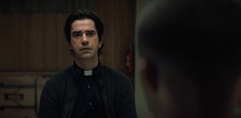 Movie still from “Midnight Mass” (2021), directed by Mike Flanagan – A man wearing a priest's collar stares into a mirror; Close Up shot, Over the shoulder angle