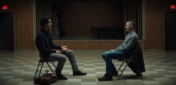 Movie still from “Midnight Mass” (2021), directed by Mike Flanagan – Two men are sitting in chairs in front of a stage; Wide shot, High angle