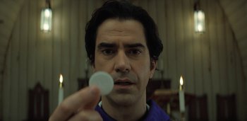 Movie still from “Midnight Mass” (2021), directed by Mike Flanagan – A person holding a round object; Close Up shot, Low angle