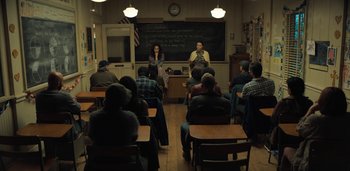 Movie still from “Midnight Mass” (2021), directed by Mike Flanagan – Two people are standing in front of a classroom full of students; Wide shot, High angle
