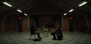 Movie still from “Midnight Mass” (2021), directed by Mike Flanagan – Two people sitting in chairs in front of a table; Wide shot, High angle
