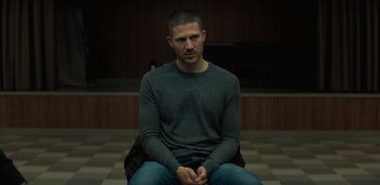 Movie still from “Midnight Mass” (2021), directed by Mike Flanagan – A man sitting on the ground in a room; Medium shot, Low angle