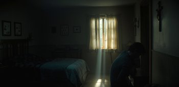 Movie still from “Midnight Mass” (2021), directed by Mike Flanagan – A person standing in front of a window in a room; Wide shot, Low angle
