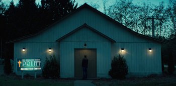 Movie still from “Midnight Mass” (2021), directed by Mike Flanagan – A man standing in front of a building at night; Extreme Wide shot, Low angle