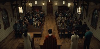 Movie still from “Midnight Mass” (2021), directed by Mike Flanagan – A group of people sitting in front of an audience in a church; Extreme Wide shot, Low angle