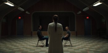 Movie still from “Midnight Mass” (2021), directed by Mike Flanagan – Three people sitting in a circle in front of a woman; Wide shot, Low angle