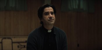 Movie still from “Midnight Mass” (2021), directed by Mike Flanagan – A man wearing a priest's outfit looking up at the ceiling; Close Up shot, Over the shoulder angle