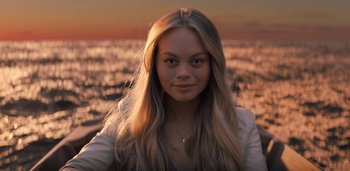Movie still from “Midnight Mass” (2021), directed by Mike Flanagan – A beautiful young woman with long blonde hair standing on top of a beach at sunset; Close Up shot, Over the shoulder angle