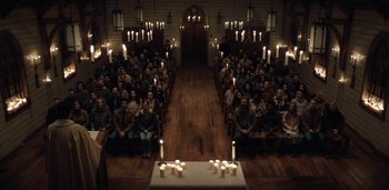 Movie still from “Midnight Mass” (2021), directed by Mike Flanagan – A group of people sitting in a room with candles on the floor; Extreme Wide shot, High angle