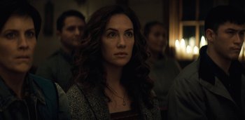 Movie still from “Midnight Mass” (2021), directed by Mike Flanagan – A woman with long curly brown hair is looking at the camera; Close Up shot, Over the shoulder angle