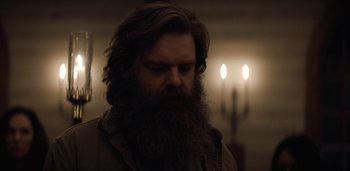 Movie still from “Midnight Mass” (2021), directed by Mike Flanagan – A man with a long beard is standing in a dimly - lit room; Close Up shot, Low angle
