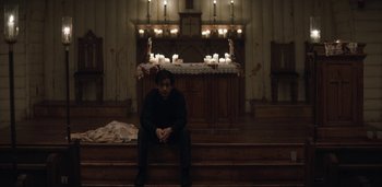 Movie still from “Midnight Mass” (2021), directed by Mike Flanagan – A man sitting on the steps in front of candles; Wide shot, Low angle