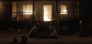Movie still from “Midnight Mass” (2021), directed by Mike Flanagan – Two people sitting on the ground in front of a house fire; Wide shot, Over the shoulder angle