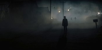 Movie still from “Midnight Mass” (2021), directed by Mike Flanagan – A person is walking in the fog on the street; Extreme Wide shot, Over the shoulder angle