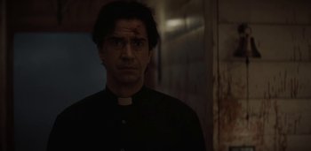 Movie still from “Midnight Mass” (2021), directed by Mike Flanagan – A man in a priest's outfit looking at the camera; Close Up shot, Low angle