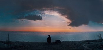 Movie still from “Midnight Mass” (2021), directed by Mike Flanagan – A person sitting on the beach watching the sunset; Extreme Wide shot, Low angle