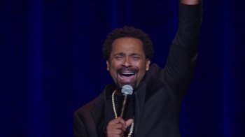 Movie still from “Mike Epps: Only One Mike” (2019), directed by Kevin Bray – A man holding a microphone up in the air; Medium shot, Overhead angle