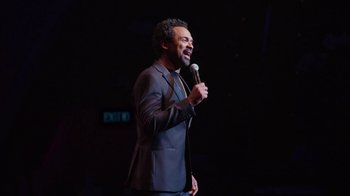 Movie still from “Mike Epps: Only One Mike” (2019), directed by Kevin Bray – A man in a black suit holding a microphone; Medium shot, High angle